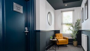 A hallway with a blue door labeled "Number Seven," a small table with a plant, a yellow armchair, and a window with blinds. - Roomy Studio Apt • Fast Wi-Fi, Parking & Laundry (Southampton)