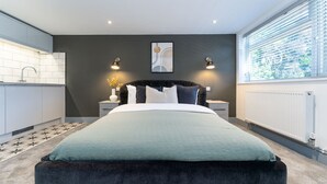 A modern bedroom with a large bed, two bedside tables, a nightstand, a window with blinds, and a radiator. - Roomy Studio Apt • Fast Wi-Fi, Parking & Laundry (Southampton)