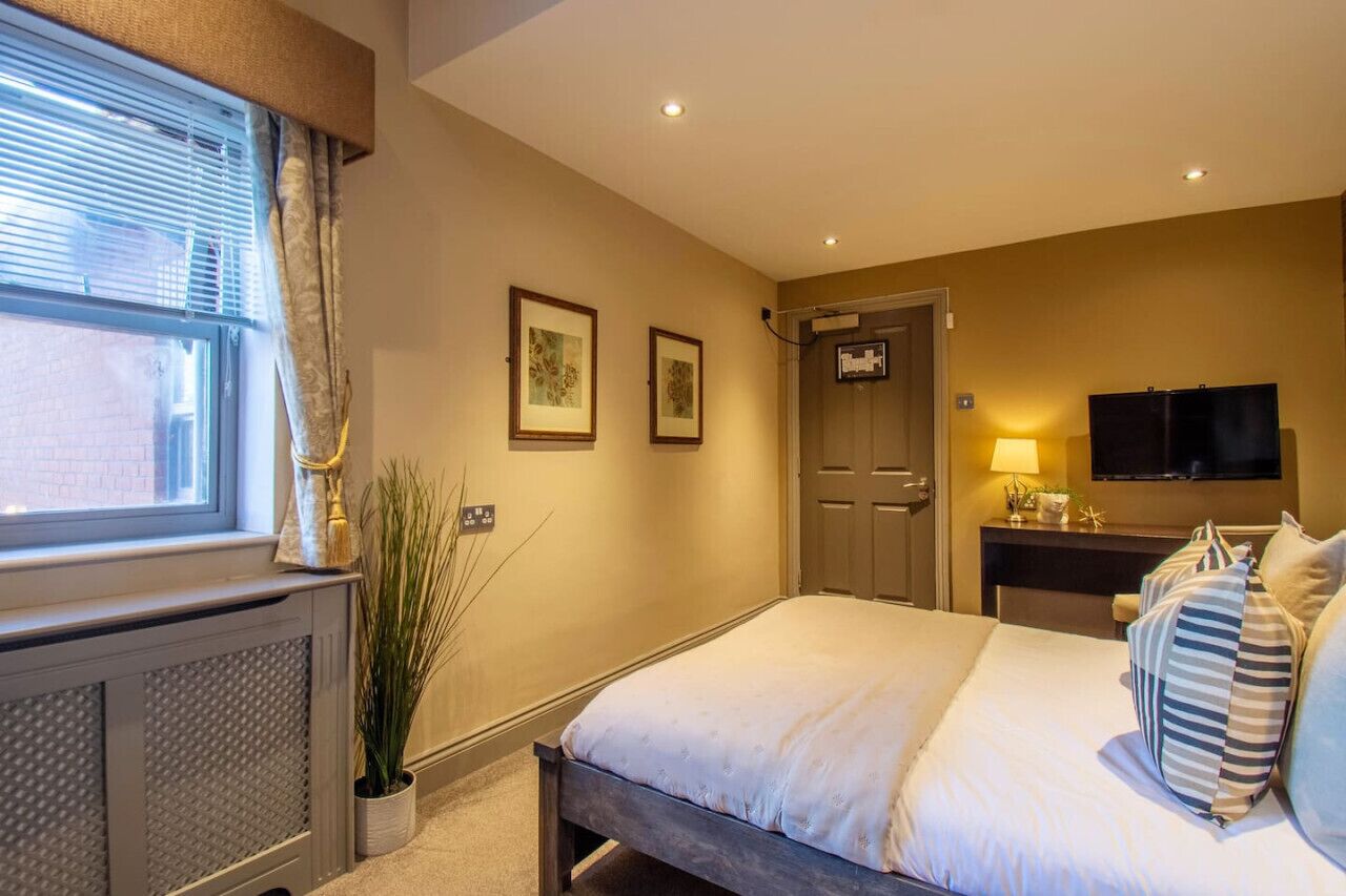 Une chambre d’hôtel avec un lit, un bureau avec une lampe, une télévision et deux tableaux encadrés au mur.