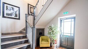 Eine Treppe mit grauer Geländer, ein gelber Sessel, ein Blumentopf und eine Tür mit grünem Ausgangsschild.