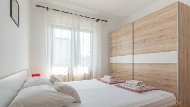 Un dormitorio con una cama, un armario de madera y una ventana con cortinas translúcidas.