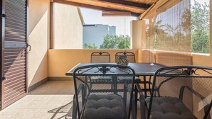 Un balcón con mesa y sillas, vista a edificios y una puerta cerrada.