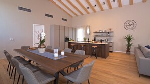 Une cuisine moderne dotée d’un îlot central, un coin repas avec une table en bois et des chaises grises, et un canapé gris dans l’espace salon.