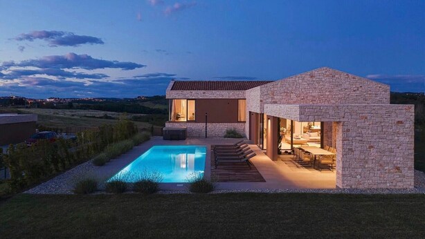 Une maison moderne dotée d’une piscine, d’une façade en pierre et offrant une vue sur la campagne.