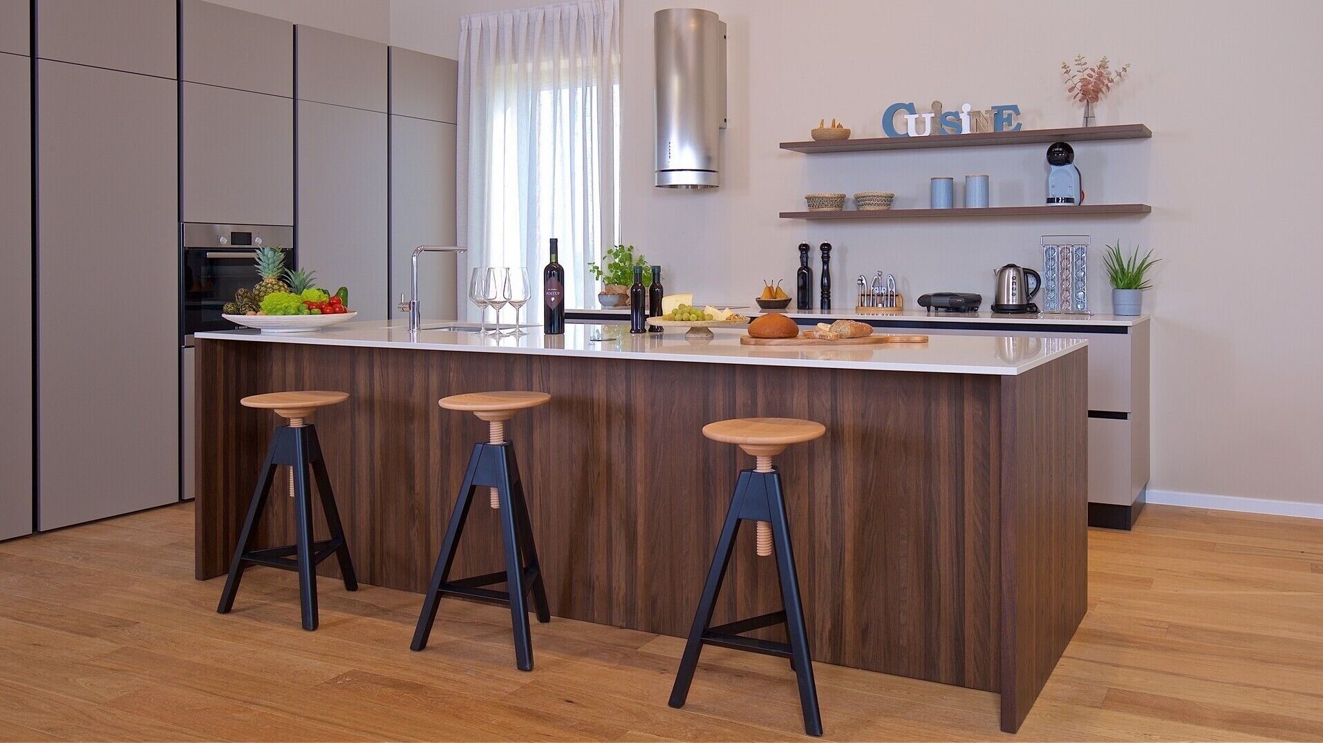 Een moderne keuken met een centraal eiland, barkrukken en een inbouwoven.
