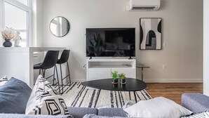 Un salon moderne avec un téléviseur à écran plat, un miroir rond et une œuvre d’art minimaliste accrochée au mur.