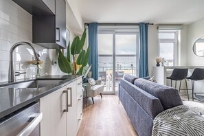 Una cucina moderna con lavello in acciaio inossidabile, un'area pranzo con un divano grigio e un tavolino, e un balcone con tende blu.