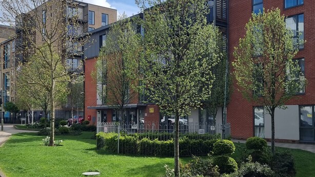 A modern building with a brick facade, surrounded by well-maintained grass and trees. - Tony's Court, Beautifully Furnished 2bedrooms Flat (London)