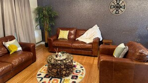 A living room with a brown leather sofa, a round coffee table made of logs, a colorful rug, and a clock on the wall. - Tony's Court, Beautifully Furnished 2bedrooms Flat (London)