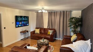 A living room with a brown leather sofa, a coffee table, and a flat-screen TV mounted on the wall. - Tony's Court, Beautifully Furnished 2bedrooms Flat (London)