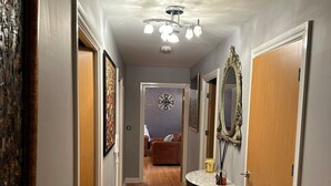 A hallway with wooden flooring, a round table with a vase and a candle, a mirror, and a clock on the wall. - Tony's Court, Beautifully Furnished 2bedrooms Flat (London)