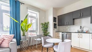 A modern kitchen with white cabinets, a stainless steel dishwasher, and a countertop with various items. - 1BR | Gym, Views | Bellevue | Sophari Parkside A (Bellevue)
