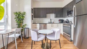 A modern kitchen with grey cabinets, stainless steel appliances, a round dining table with chairs, and a potted plant. - 1BR | Gym, Views | Bellevue | Sophari Parkside A (Bellevue)