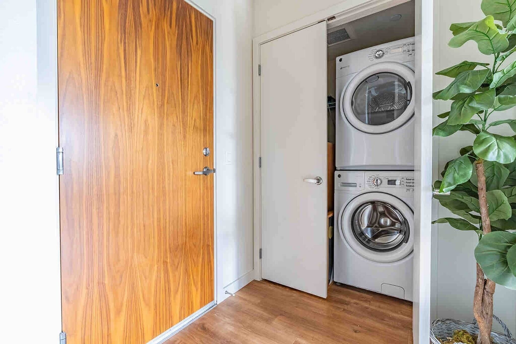 A laundry room with two stacked washing machines and a wooden door.