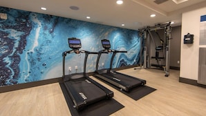 A fitness room with two treadmills, a wall mural, and a weightlifting area. - 1BR | Gym, Views | Bellevue | Sophari Parkside A (Bellevue)