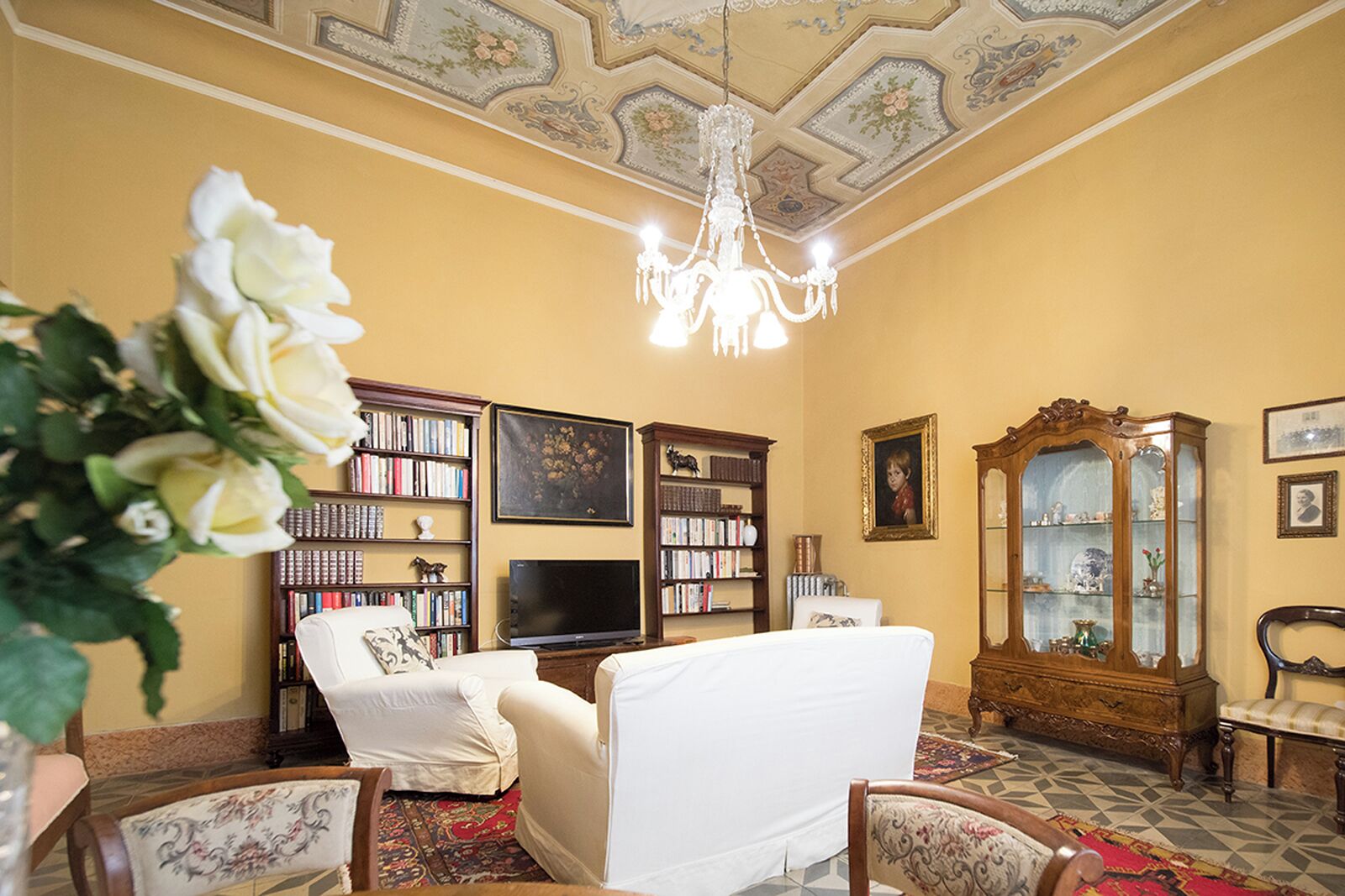 A living room with a chandelier, bookshelves, a television, and a cabinet.
