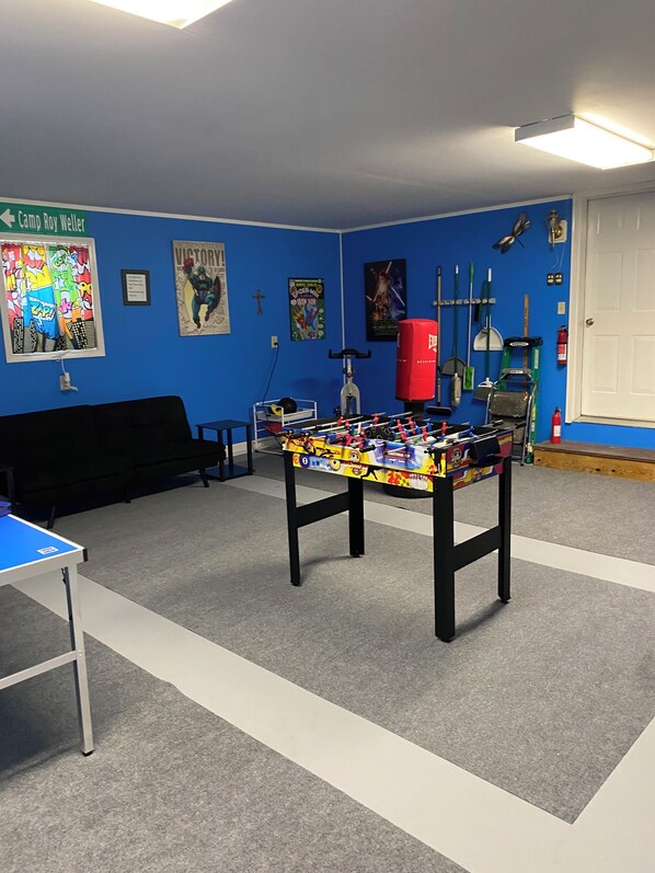 A room with a foosball table, a blue wall with posters, a black couch, and a door.