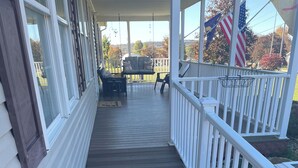 A wooden deck with a white railing, a hanging chair, and a basketball hoop.