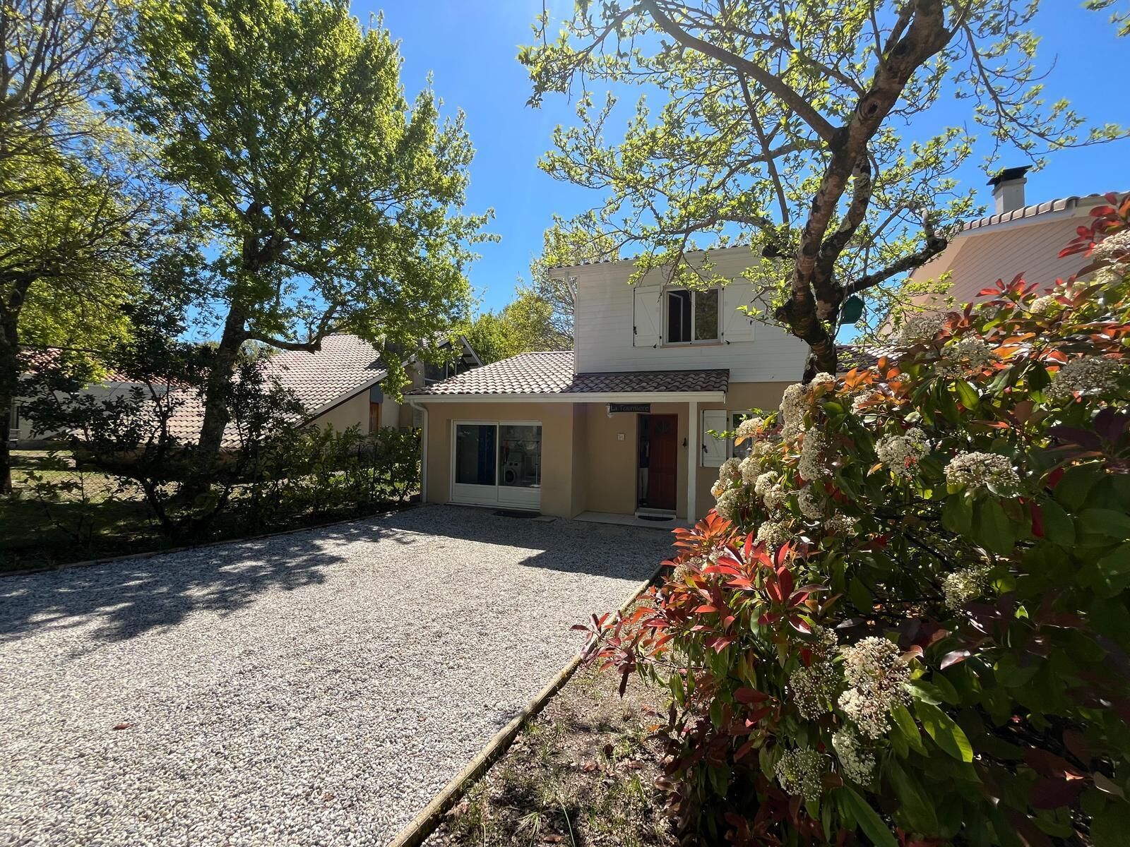 Une maison à deux étages avec une allée en gravier et un jardin agrémenté de plantes à fleurs.