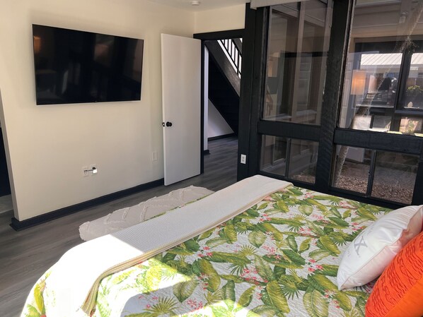 Un dormitorio con cama, televisor, puerta y ventana.