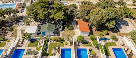 An aerial view of a resort with multiple swimming pools, a beach, and lush greenery.