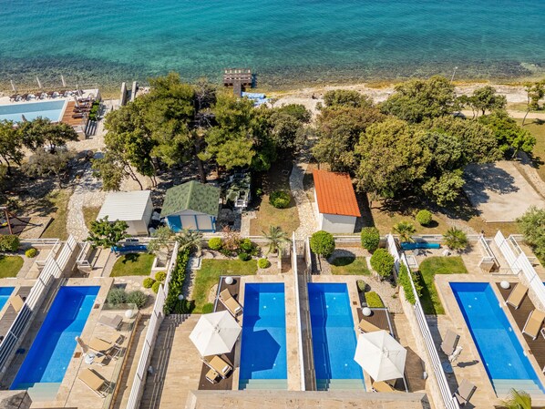 An aerial view of a resort with multiple swimming pools, a beach, and lush greenery.