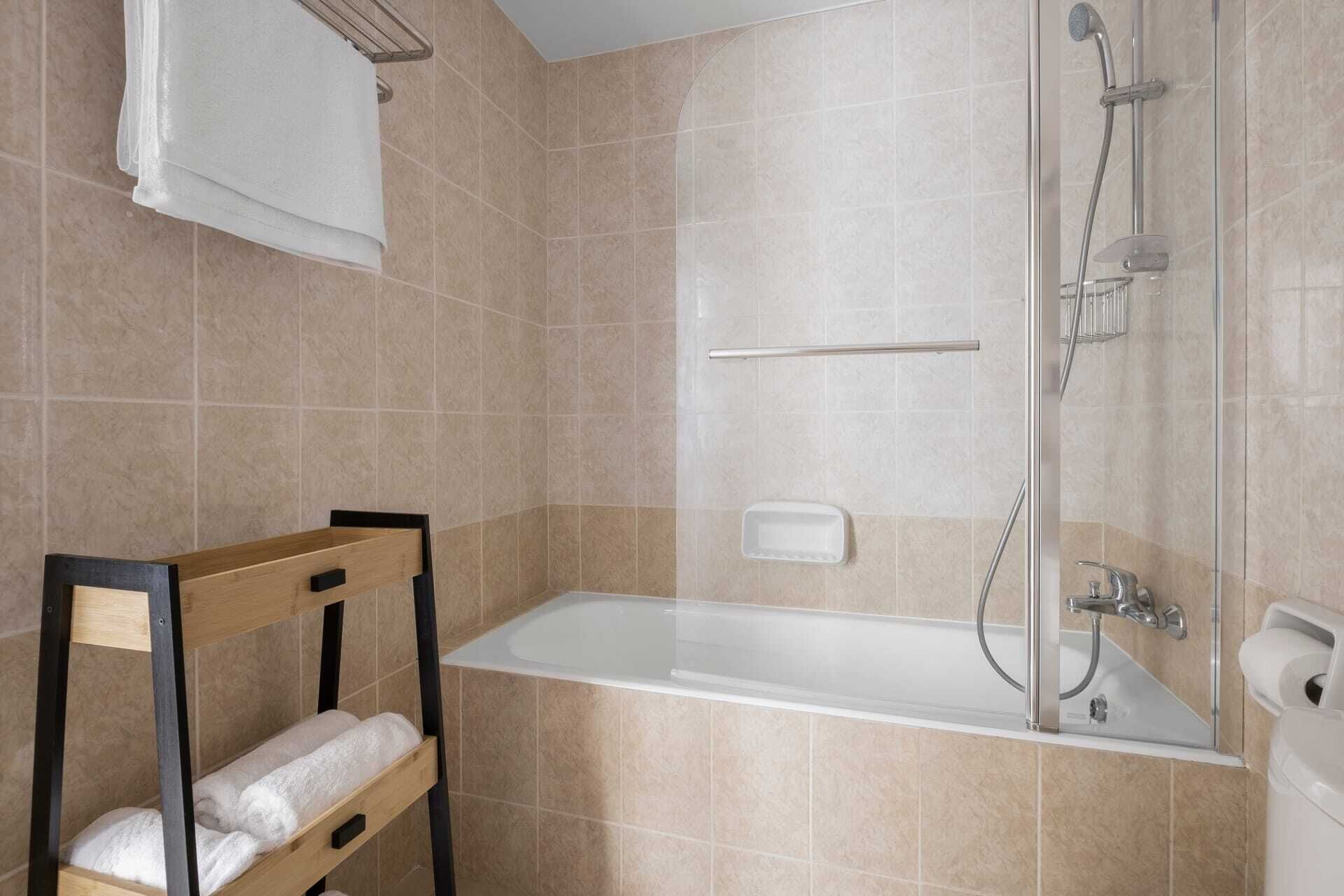 A modern bathroom with a bathtub, a shower, and a wooden chair with a towel.