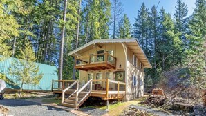 A two-story cabin with a balcony, surrounded by trees.