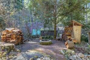 A rustic outdoor area with a fire pit, stacks of firewood, and a wooden structure.