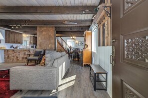 Un amplio espacio de sala con un sofá grande de color gris, una mesa de centro de madera y una alfombra roja. Una escalera conduce a un nivel superior con barandilla de madera.