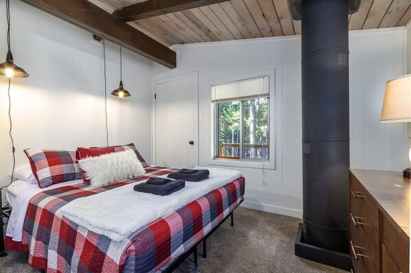 Un dormitorio con cama, ventana, chimenea y techo de madera.