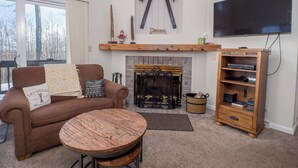 A cozy living room with a fireplace, a sofa, a coffee table, and a TV. - 8280 The peak- Hot tub, ski in/ ski out, Pool table, Golf course, fire pit (Clymer)