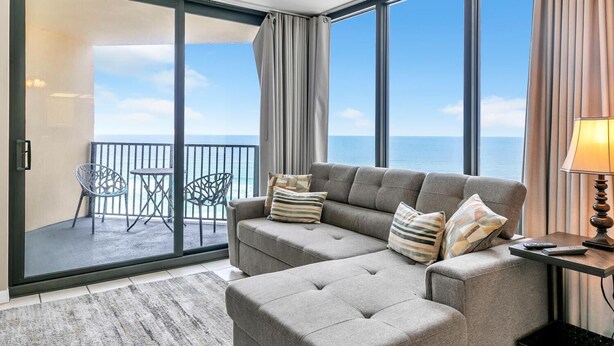 Ein Balkon mit Meerblick, ein graues Sofa mit gestreiften Kissen und ein kleiner Tisch mit einer Lampe.