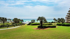 A well-maintained lawn with a pathway leading to a pool area, surrounded by palm trees and a view of the ocean. - 🚢Steps to Private Beach-Gulf Views-2 Pools with Waterfall-1BR Edgewater #303🚢 (Miramar Beach)