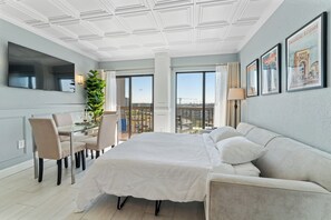 Ein Hotelzimmer mit einem großen Bett, einem Schreibtisch, einem Stuhl, einer Topfpflanze und einem Balkon mit Blick.