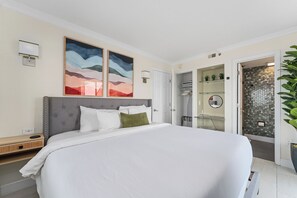 A modern bedroom with a large bed, a walk-in closet, and a bathroom with a glass shower. - Terrace Suite with Epic Fireworks View (Orlando)