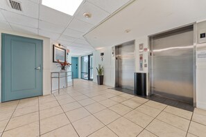 Eine moderne Lobby mit Fliesenboden, einer blauen Tür, einem Empfangstresen, einem Blumentopf und einem Aufzug.
