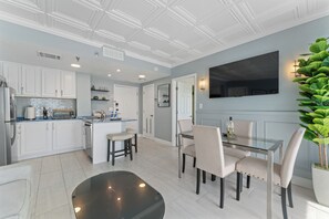 Une cuisine moderne avec des meubles blancs, un îlot central et un coin repas comprenant une table et des chaises en verre.