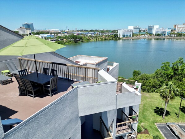 Una terraza en la azotea con mobiliario exterior, vista a un lago y edificios circundantes.