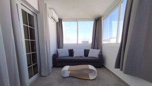 En moderne stue med en grå sofa, et træbord og store vinduer med gardiner.