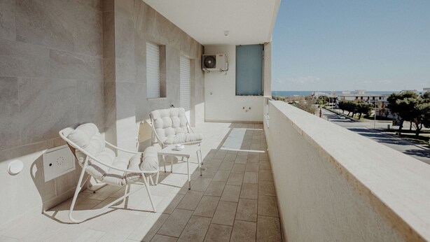 A balcony with two white chairs and a table, a wall-mounted air conditioner, and a view of the cityscape. - Moments by Monholiday (Monopoli)