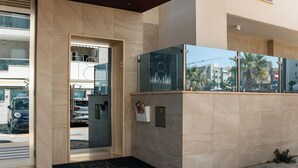 A modern building entrance with a glass door, a black mat with a logo, and a small mailbox. - Moments by Monholiday (Monopoli)