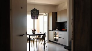 A modern kitchen with a dining area, featuring a hanging light fixture, a built-in oven, and a large window providing natural light. - Moments by Monholiday (Monopoli)