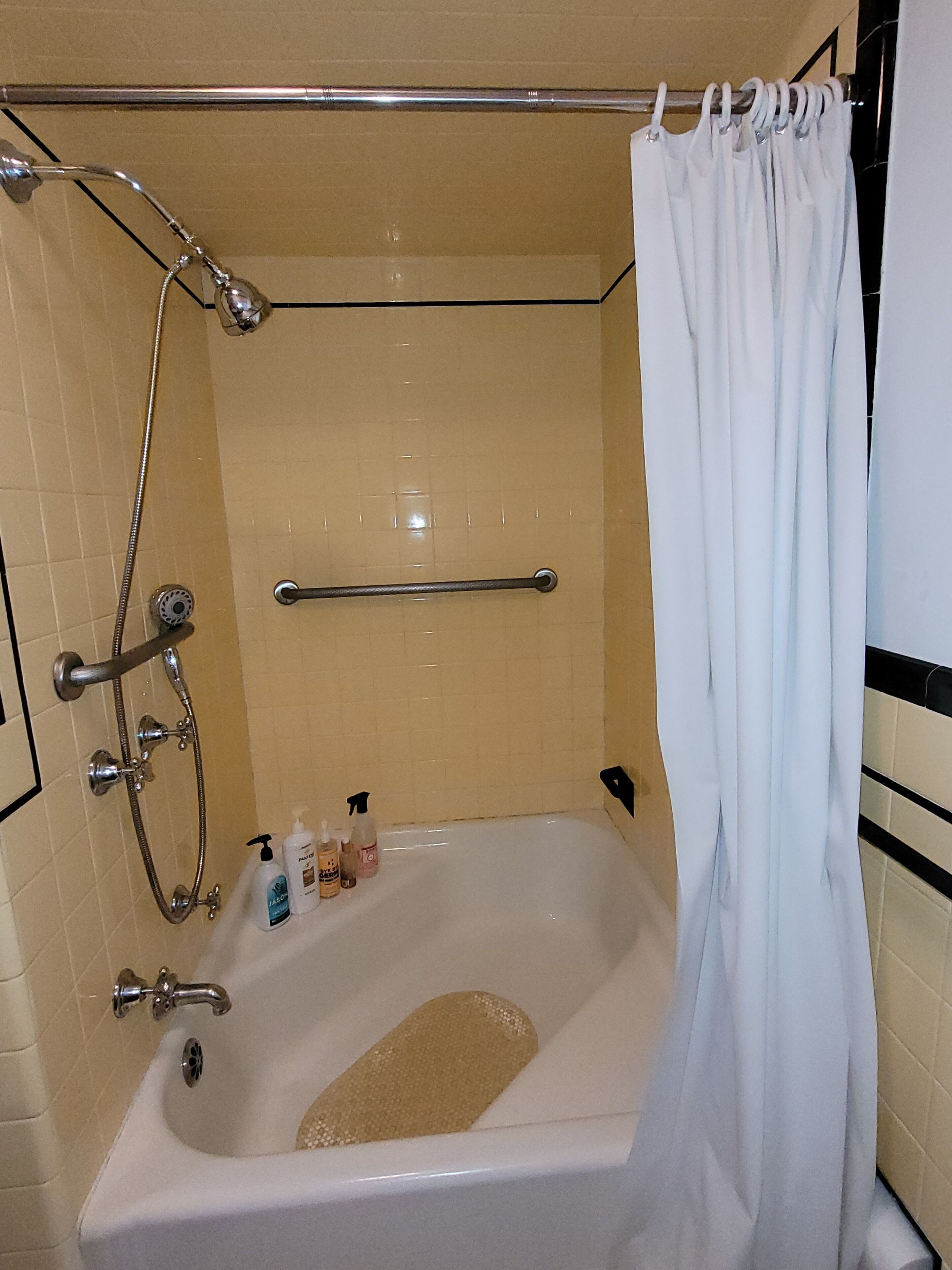 Een badkamer met een badkuip, een douche en een handgreep. Er liggen toiletartikelen op de badrand.