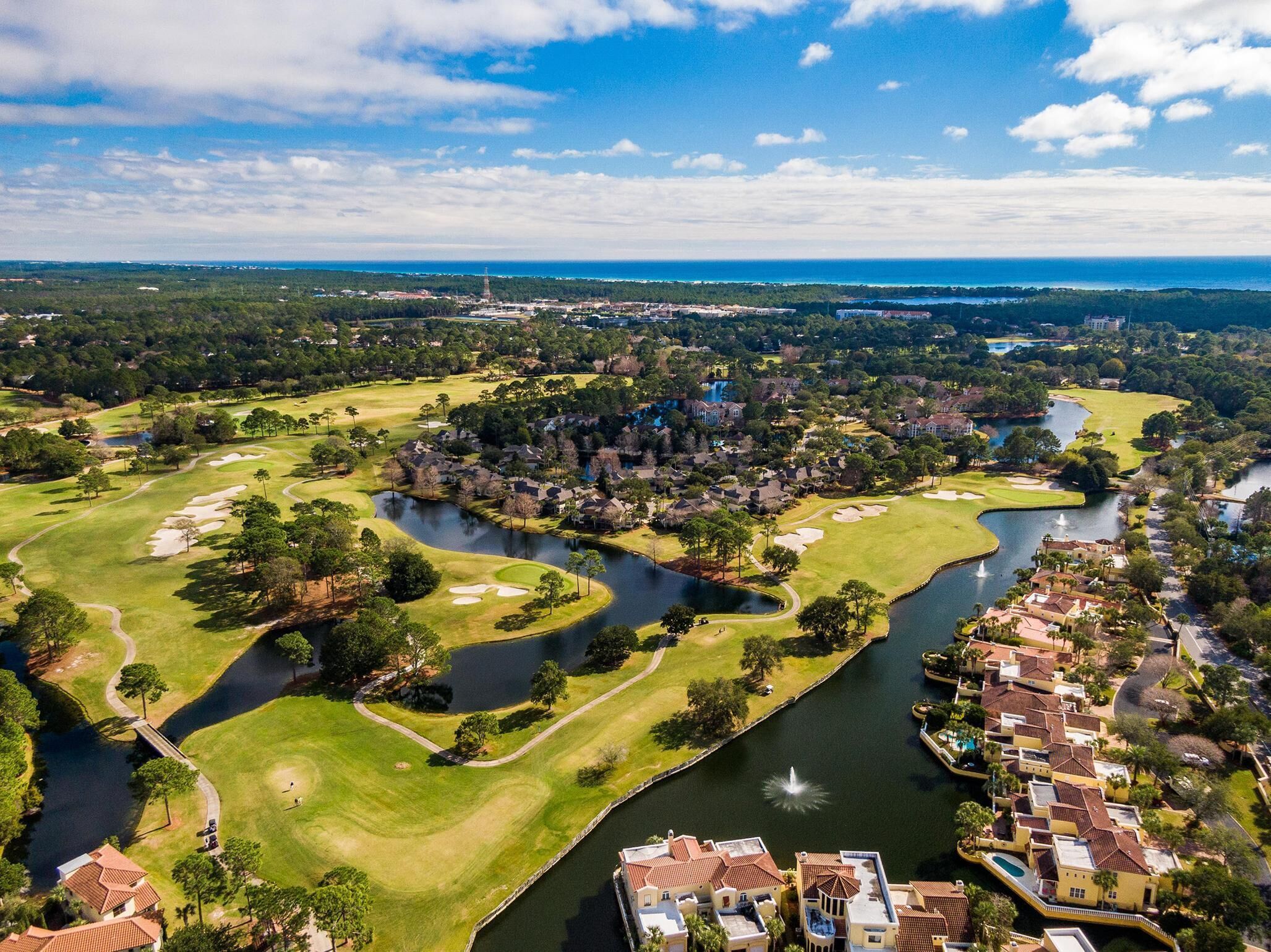 Luchtbeeld van een golfbaan met een meer, omringd door woongebouwen en een verre stadsachtergrond.