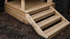 A wooden outdoor structure with horizontal slats, a ramp, and a white object inside.
