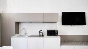 Eine kompakte Küchenzeile mit Spüle, Wasserkocher, Mikrowelle und einem an der Wand befestigten Flachbildfernseher.