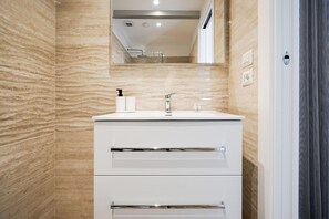 Et moderne badeværelse med en marmorvæg, et hvidt toiletbord med spejl og et bruseområde.