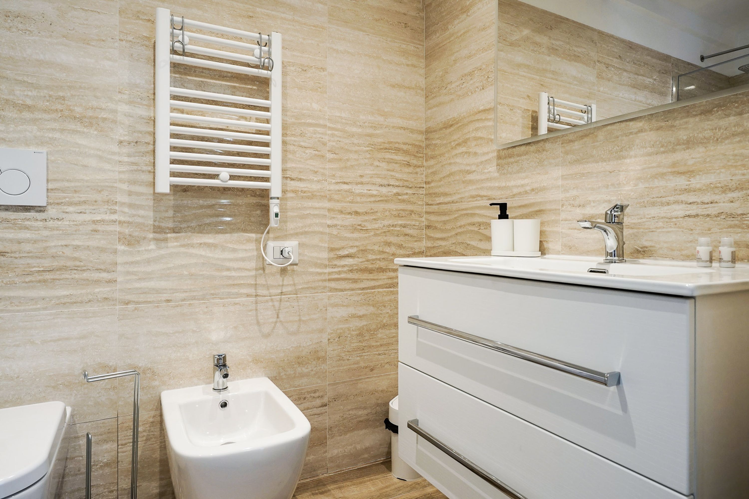Une salle de bain moderne avec un bidet, un lavabo blanc avec un miroir et un porte-serviettes.