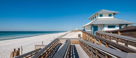A wooden boardwalk leading to a beach with a lifeguard tower.